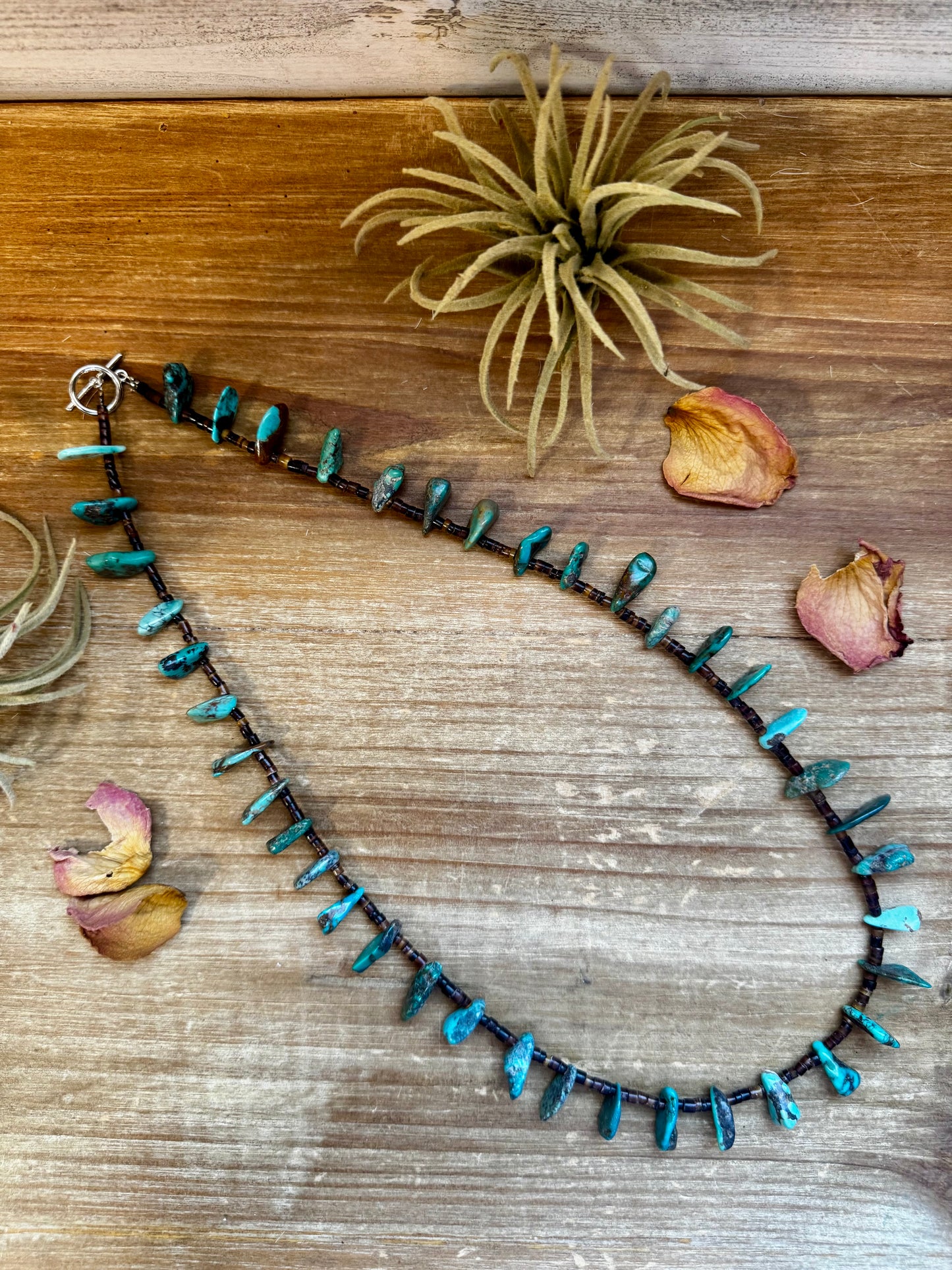 Close-up of a 4-inch long handmade earring with 3-inch extender, featuring 3mm dark shell beads and a real turquoise teardrop pendant. Silver-plated finish. Each turquoise stone is unique. Made in the USA by The Bijoux FAB.