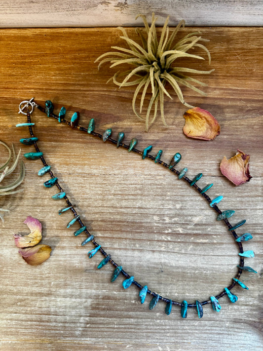 Close-up of a 4-inch long handmade earring with 3-inch extender, featuring 3mm dark shell beads and a real turquoise teardrop pendant. Silver-plated finish. Each turquoise stone is unique. Made in the USA by The Bijoux FAB.