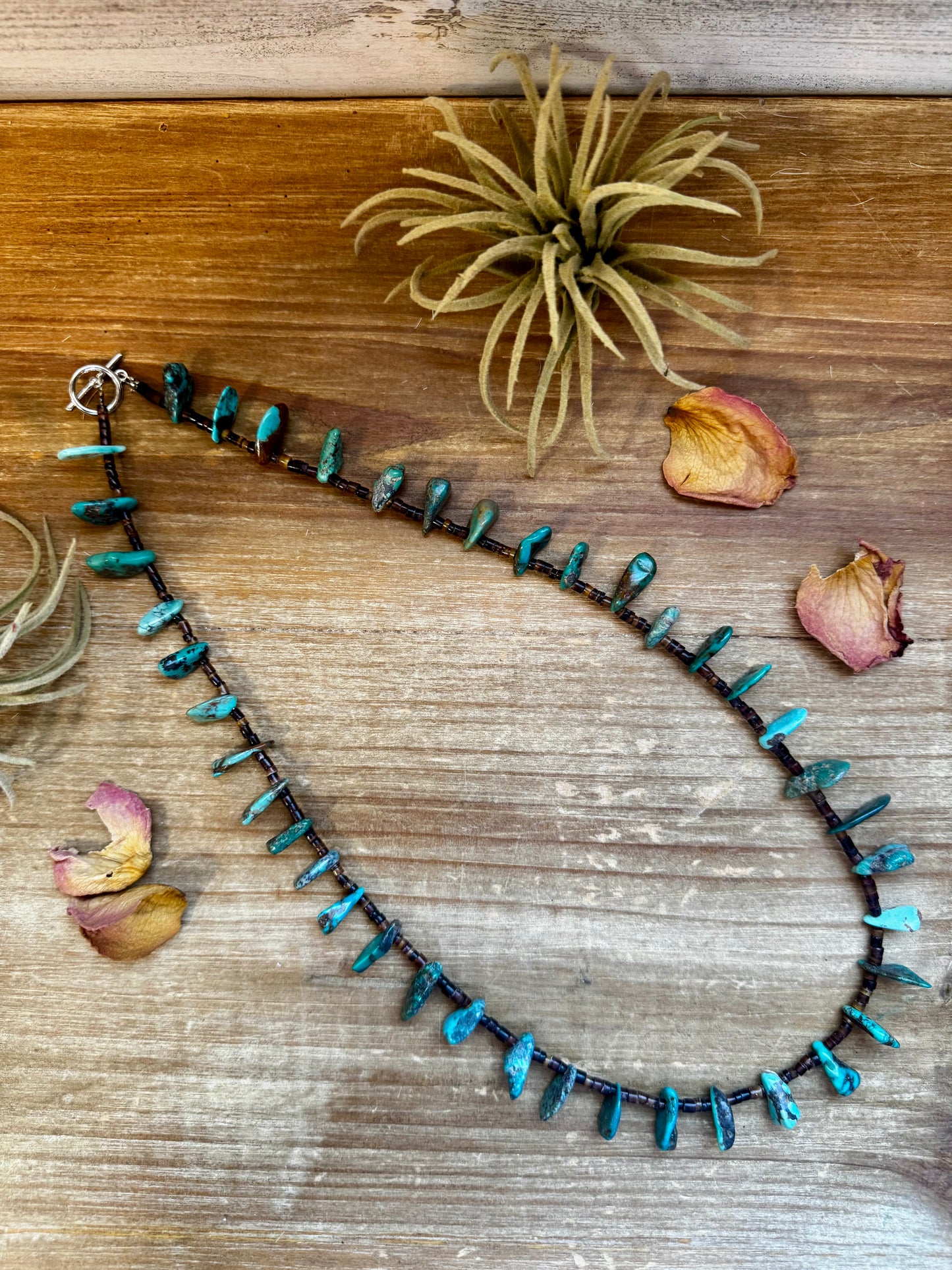 Close-up of a 4-inch long handmade earring with 3-inch extender, featuring 3mm dark shell beads and a real turquoise teardrop pendant. Silver-plated finish. Each turquoise stone is unique. Made in the USA by The Bijoux FAB.