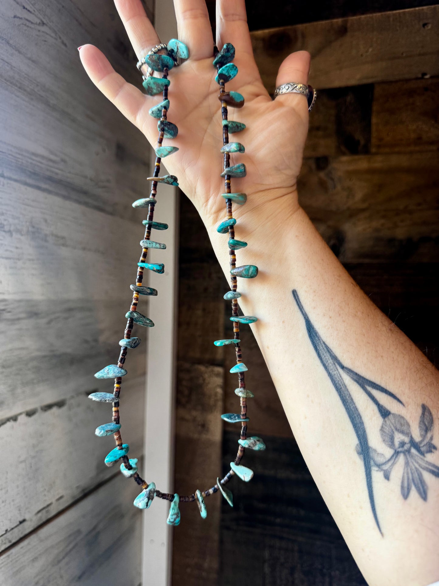 Close-up of a 4-inch long handmade earring with 3-inch extender, featuring 3mm dark shell beads and a real turquoise teardrop pendant. Silver-plated finish. Each turquoise stone is unique. Made in the USA by The Bijoux FAB.